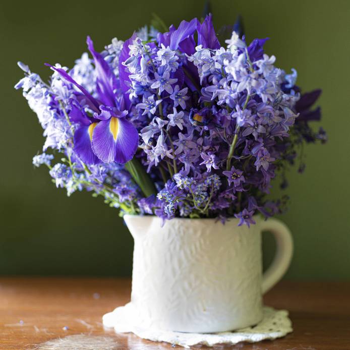 Blue flowers in a white jug upon a wood table