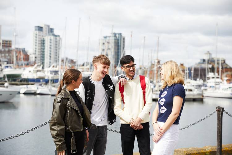 A group of students standing by Ipswich waterfront, with boats in the background