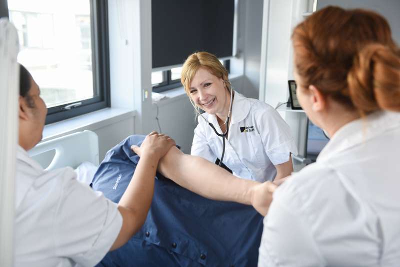 Nursing student in white uniform smiling over patient