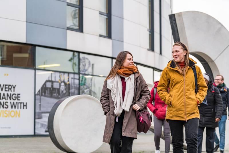 Students outside walking outside the Waterfront Building, near the Question Mark statue