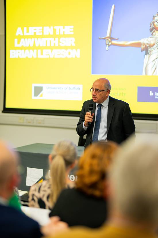 Sir Brian Leveson in front of a presentation screen