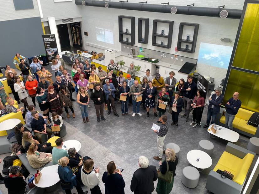A photo looking down on the Suffolk Reflections book launch event in The Atrium. Simon Peachey is giving a speech to the guests gathered around