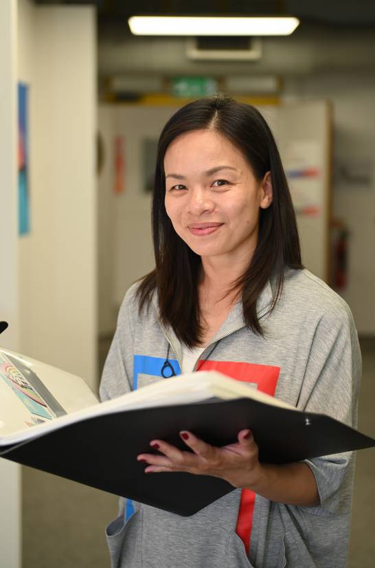 Sammi Wong smiling and holding open her final year portfolio