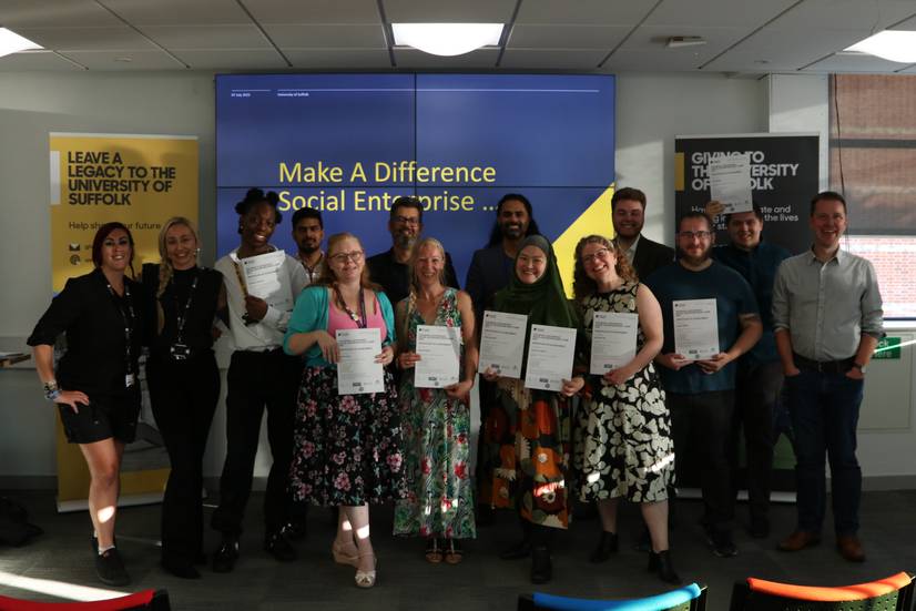 Students and staff involved in the Make A Difference Social Enterprise Bootcamp final, summer 2023. The group is gathered together and holding certificates in front of the projector screen