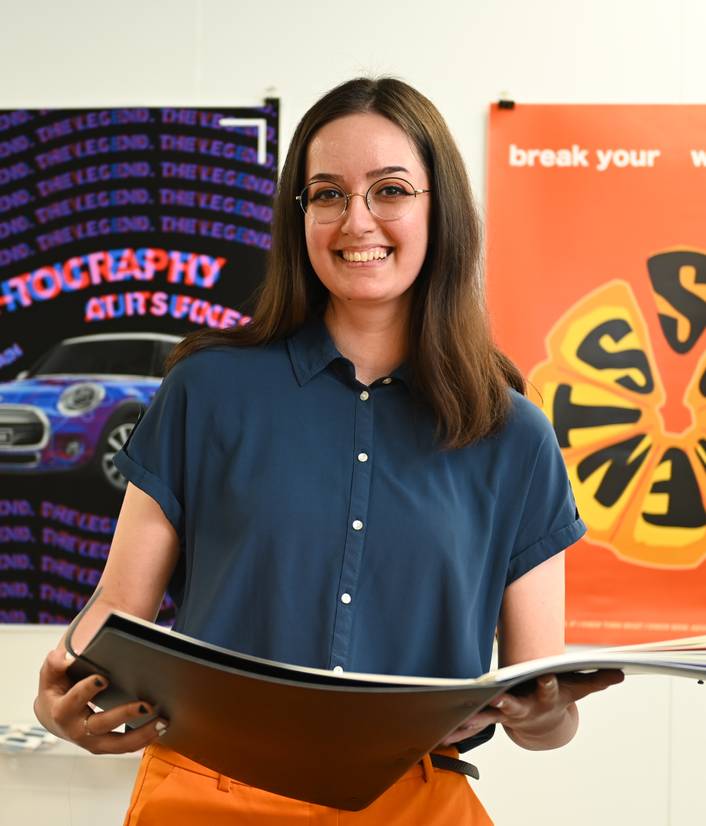 A photo of Maria-Teodora Dragomir holding her arts degree show portfolio
