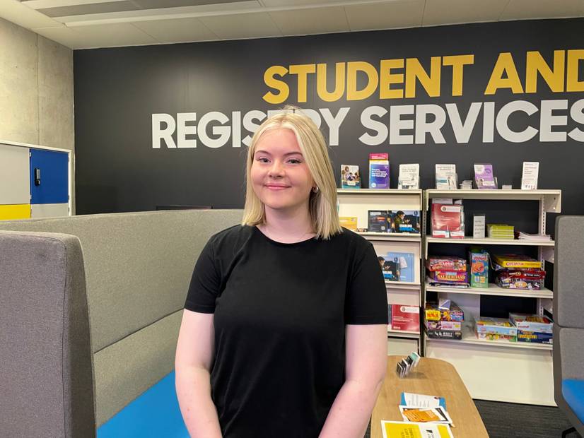 Zoe Whent, a student who came through Clearing, standing in the Waterfront Building with learning resources behind her