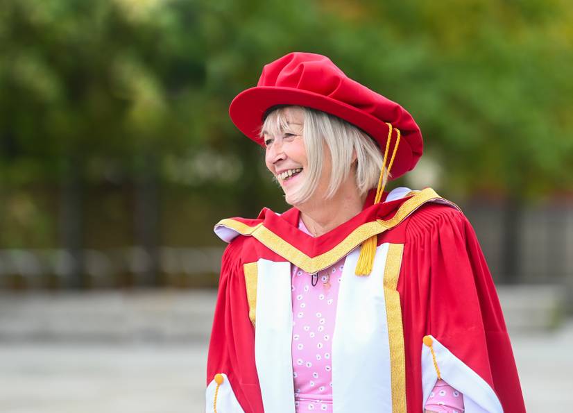Ann Osborn dressed in graduation robes standing outside the university smiling