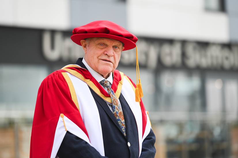 Charlie Haylock standing outside a Ӱ sign wearing graduation robes