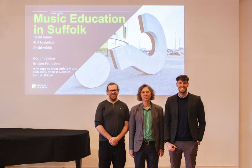 Left to right: David Atkins, David James and Phil Nicholson standing in front of a power point slide introducing their music education report. The event was held at Snape Maltings venue