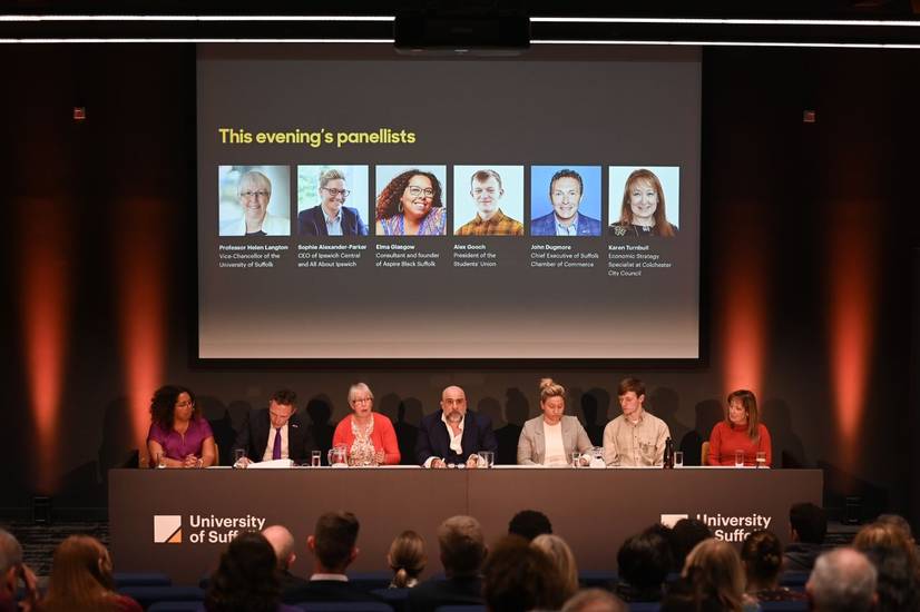 The panel for the Spotlight Suffolk event lined up at a desk, in front of an audience seated in a lecture theatre. Behind the panel is a powerpoint screen with the names of the speakers