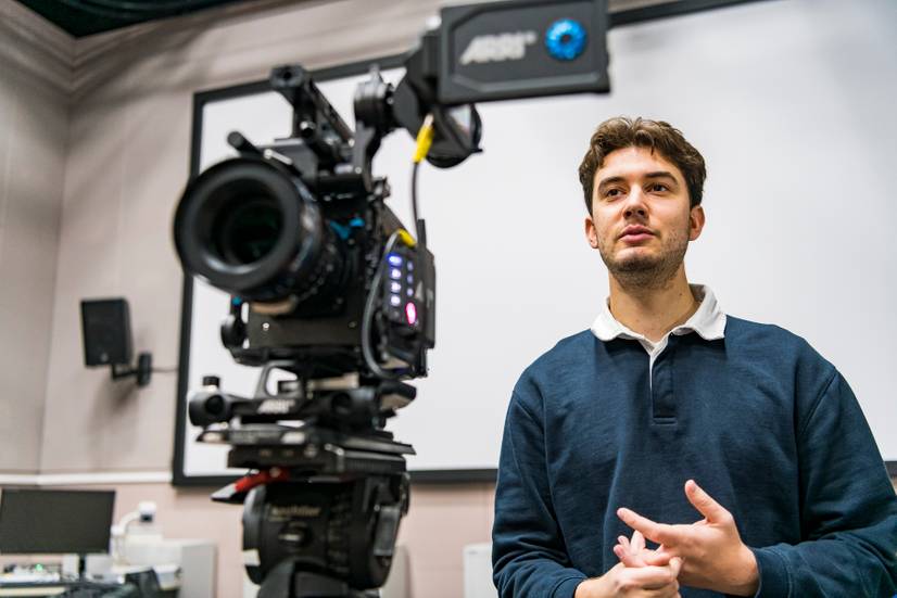 A student standing next to a video camera