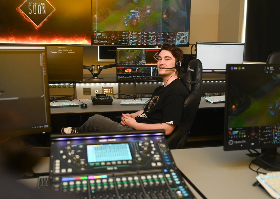 A male student sitting at the broadcast desk wearing a headset